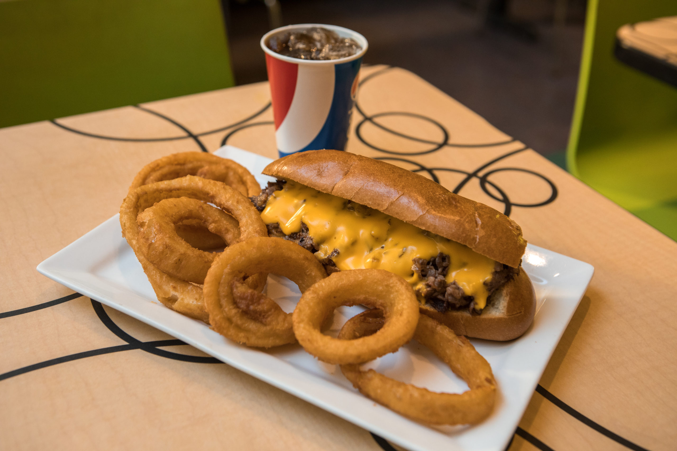 Philly cheesesteak sandwich with cola and onion rings